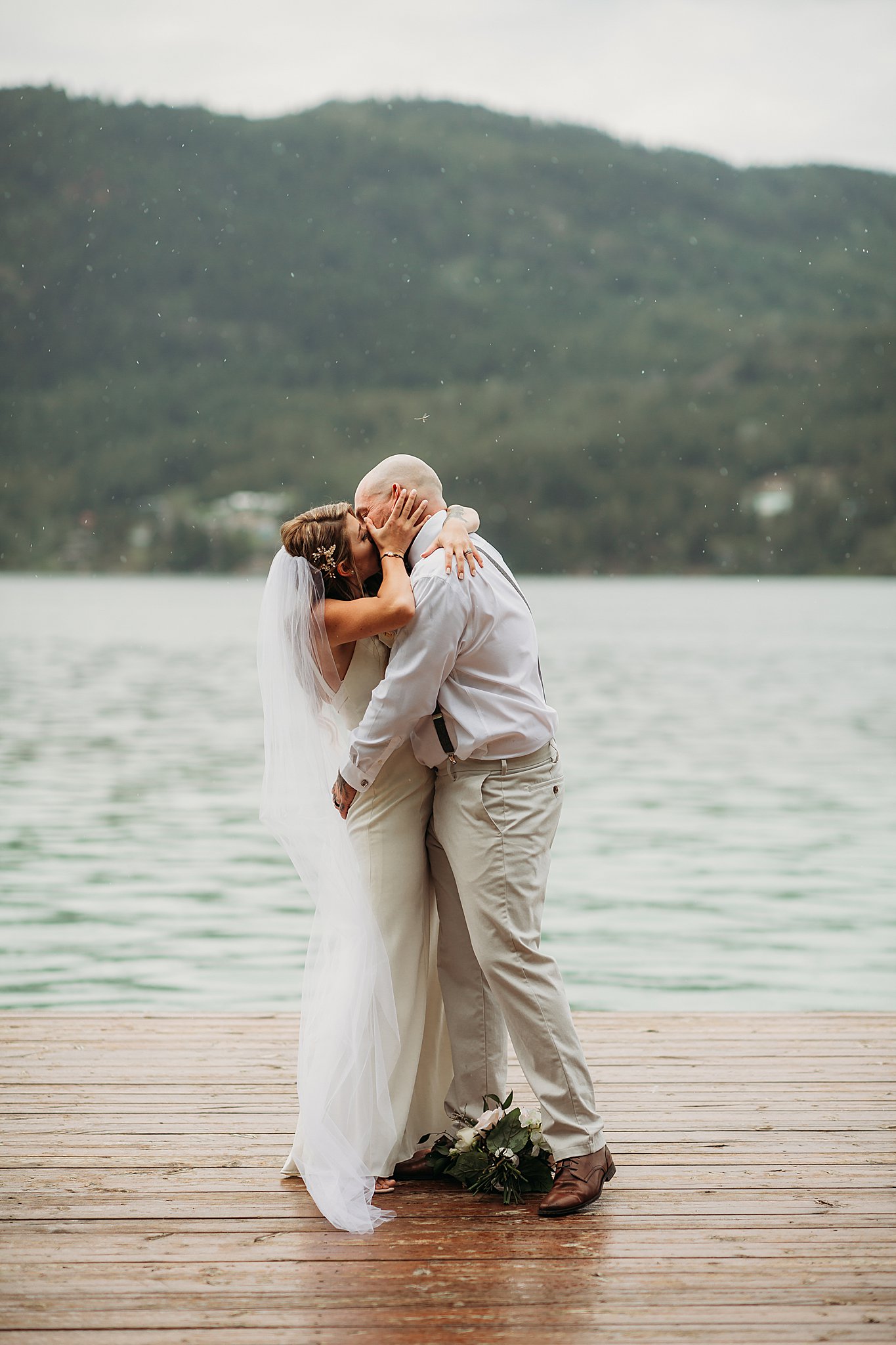 white lake wedding first kiss on the dock in the rain