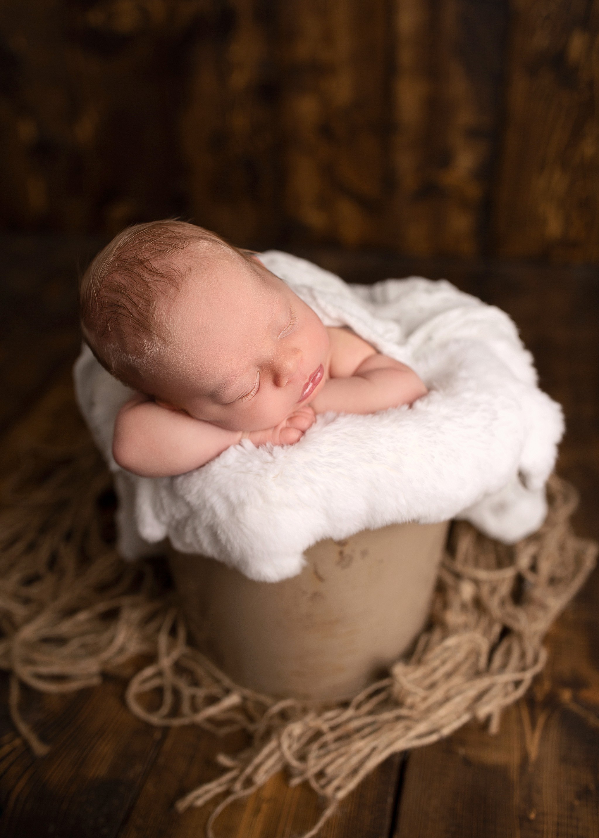 A sleeping newborn boy is posed in a bucket by an experience newborn photographer