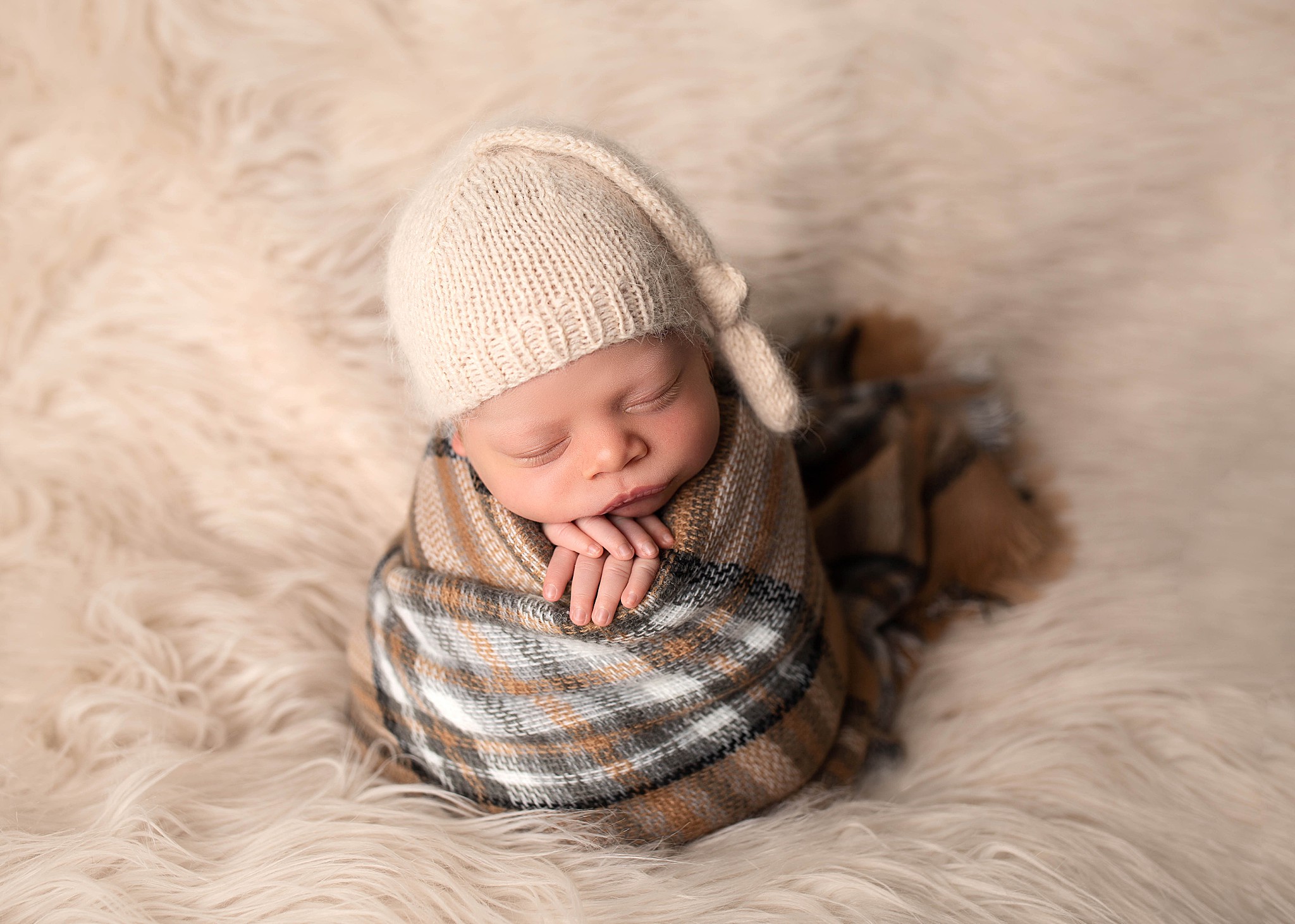A kamloops newborn photographer captures a sleeping baby boy who is wrapped up in a plaid blanket