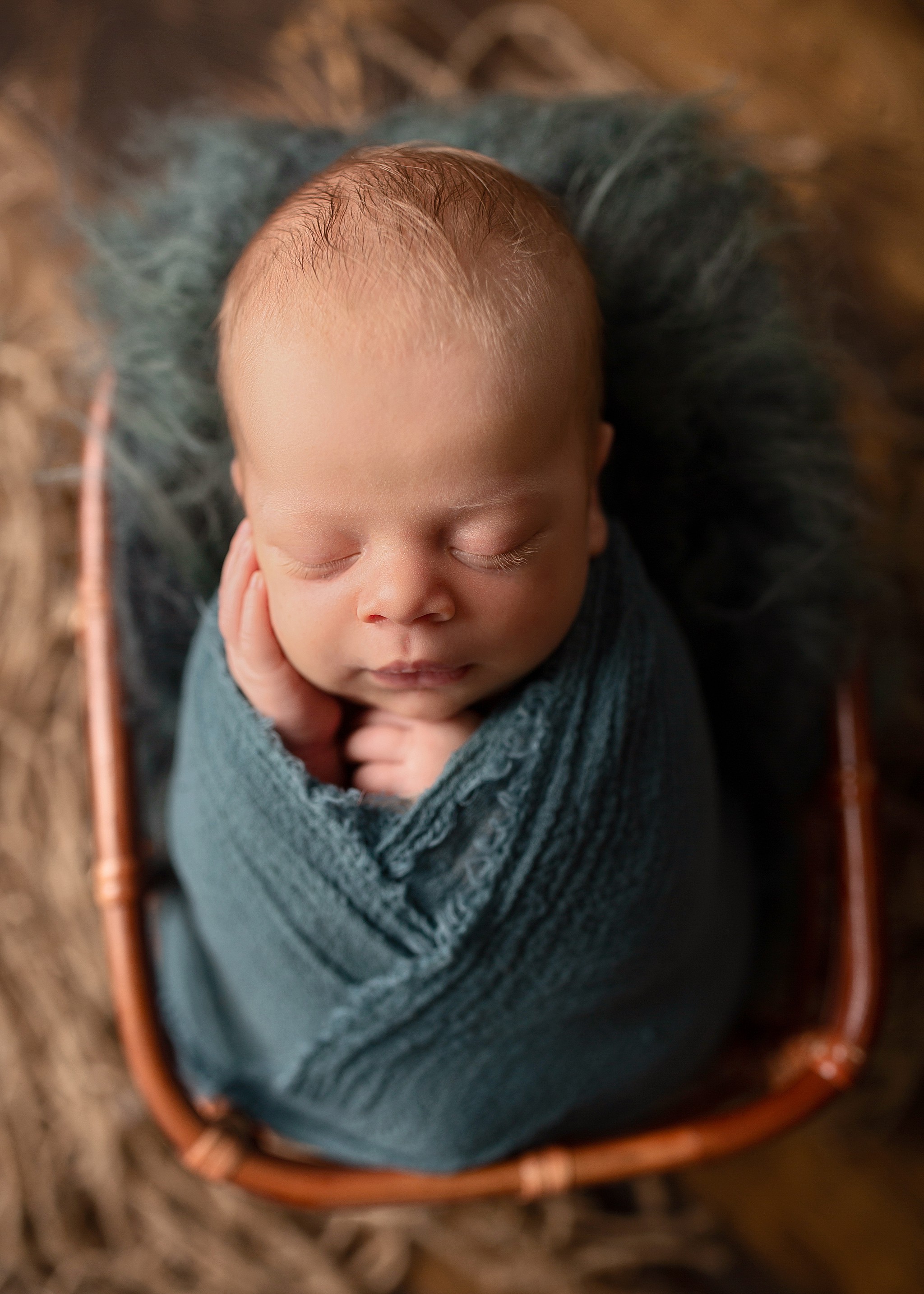 a kamloops newborn photographer captures a sleeping newborn boy in a basket in a teal coloured wrap.