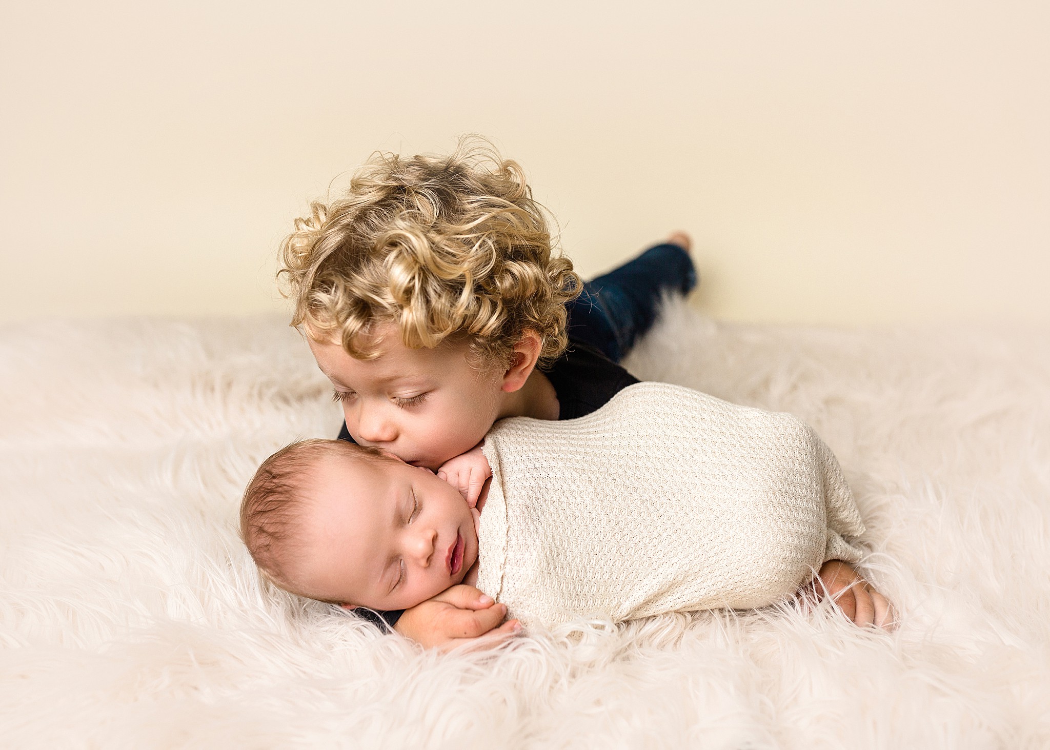 a sleeping baby boy posed by a kamloops newborn photographer in his big brothers arms