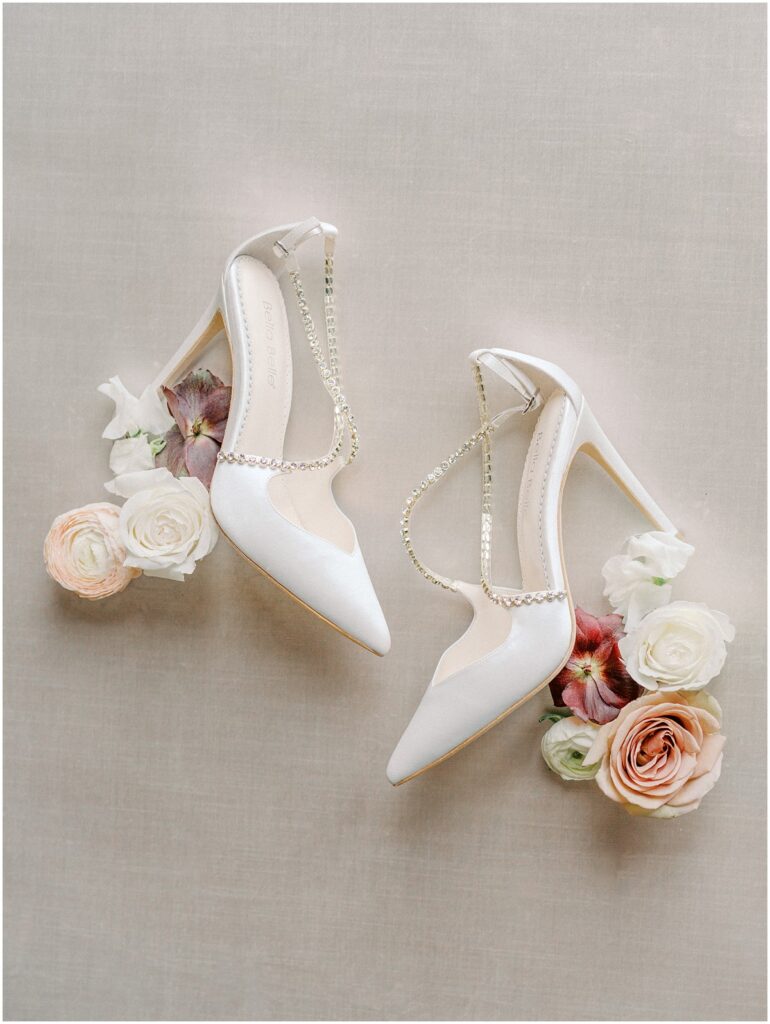 A image of white wedding shoes with flowers places around them.