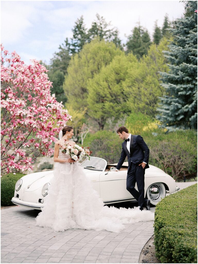 A bride and groom stand in front of a vintage car for a European Inspired wedding editorial at Chateau Okanagan.